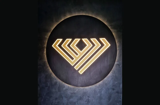 Zlaté geometrické logo na tmavom kruhovom podklade s halo podsvietením