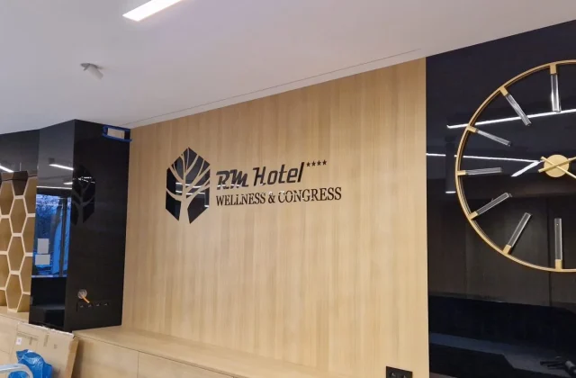 Priestorové čierne logo a nápis RM Hotel Wellness & Congress na drevenej stene recepcie