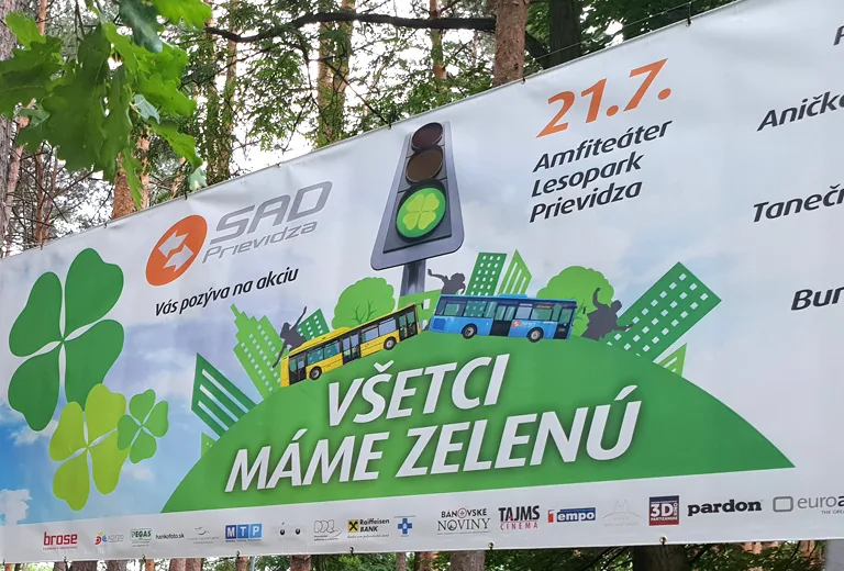 Veľkoplošný banner s pozvánkou na podujatie napnutý medzi stromami v lesoparku