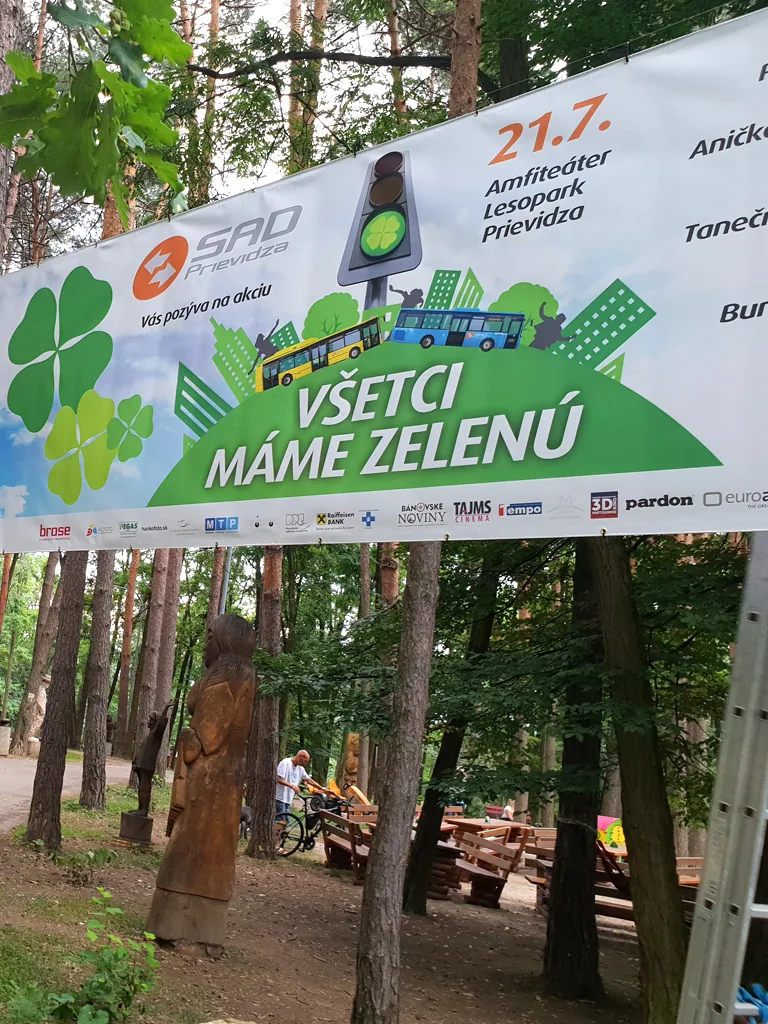 Reklamný banner s pozvánkou na kultúrne podujatie napnutý medzi stromami