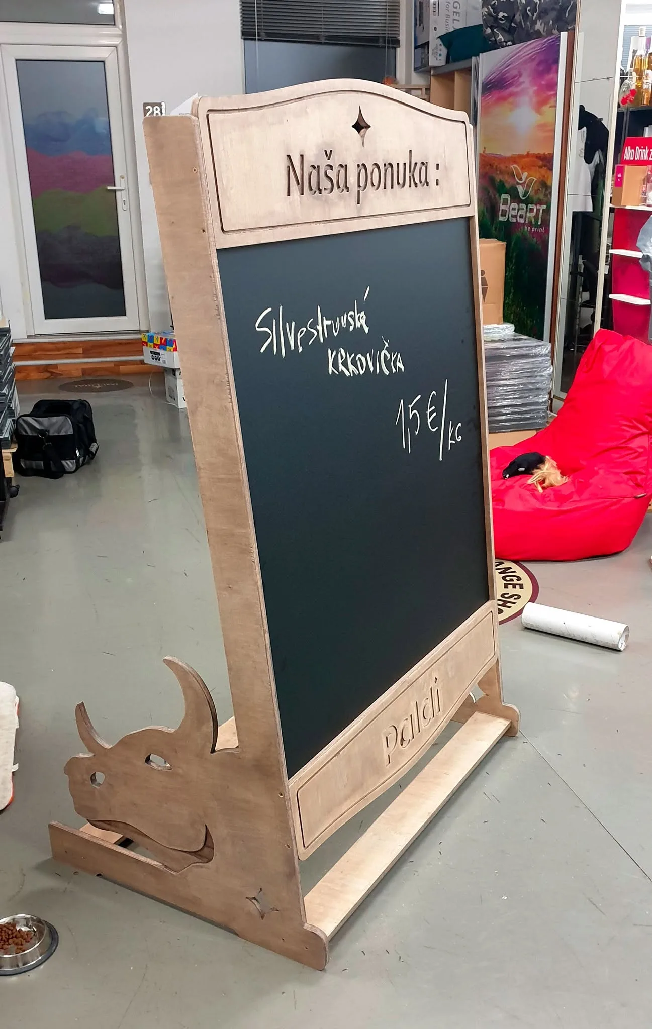 Hotový drevený reklamný stojan s čiernou tabuľovou plochou, popísaný kriedou, s frézovanou hlavou býka