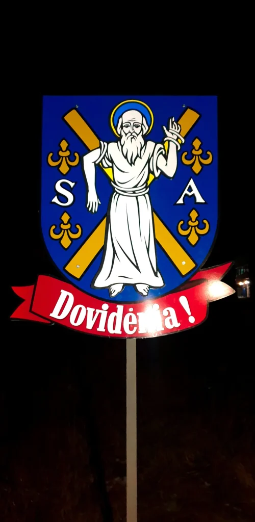 Tabuľa Dovidenia s obecným erbom na stĺpiku v noci, reflexné prvky svietia