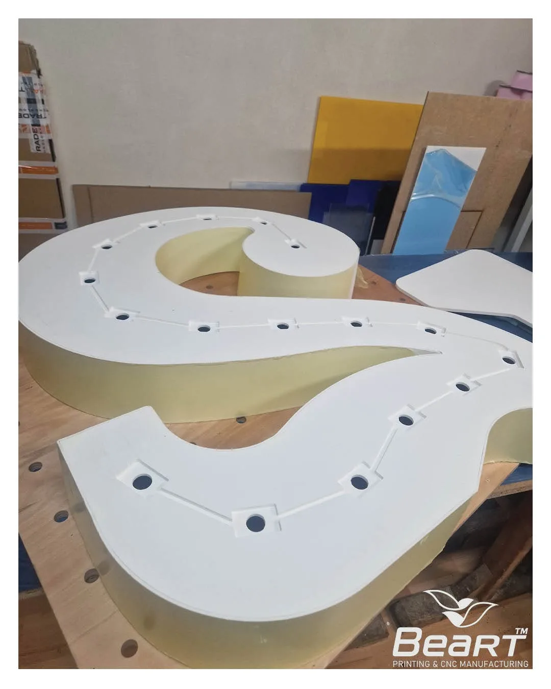 Rozrobené biele diely priestorového čísla s vyvŕtanými otvormi pre LED žiarovky na CNC stole
