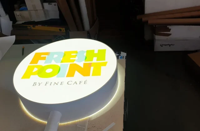 Rozsvietený okrúhly svetelný box s plnofarebným logom kaviarne, nasvietený v dielni pred montážou
