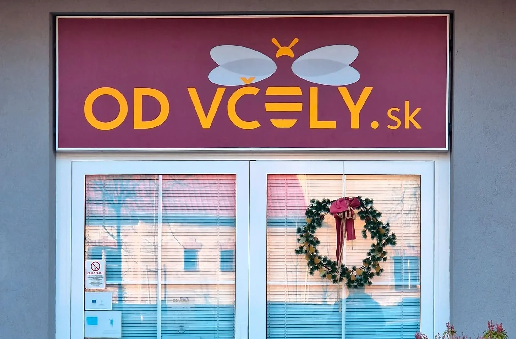 Bordový svetelný panel s logom a nápisom nad preskleným vchodom do predajne, denný záber