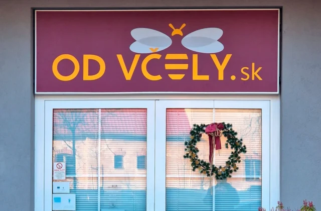 Bordový svetelný panel s logom a nápisom nad preskleným vchodom do predajne, denný záber
