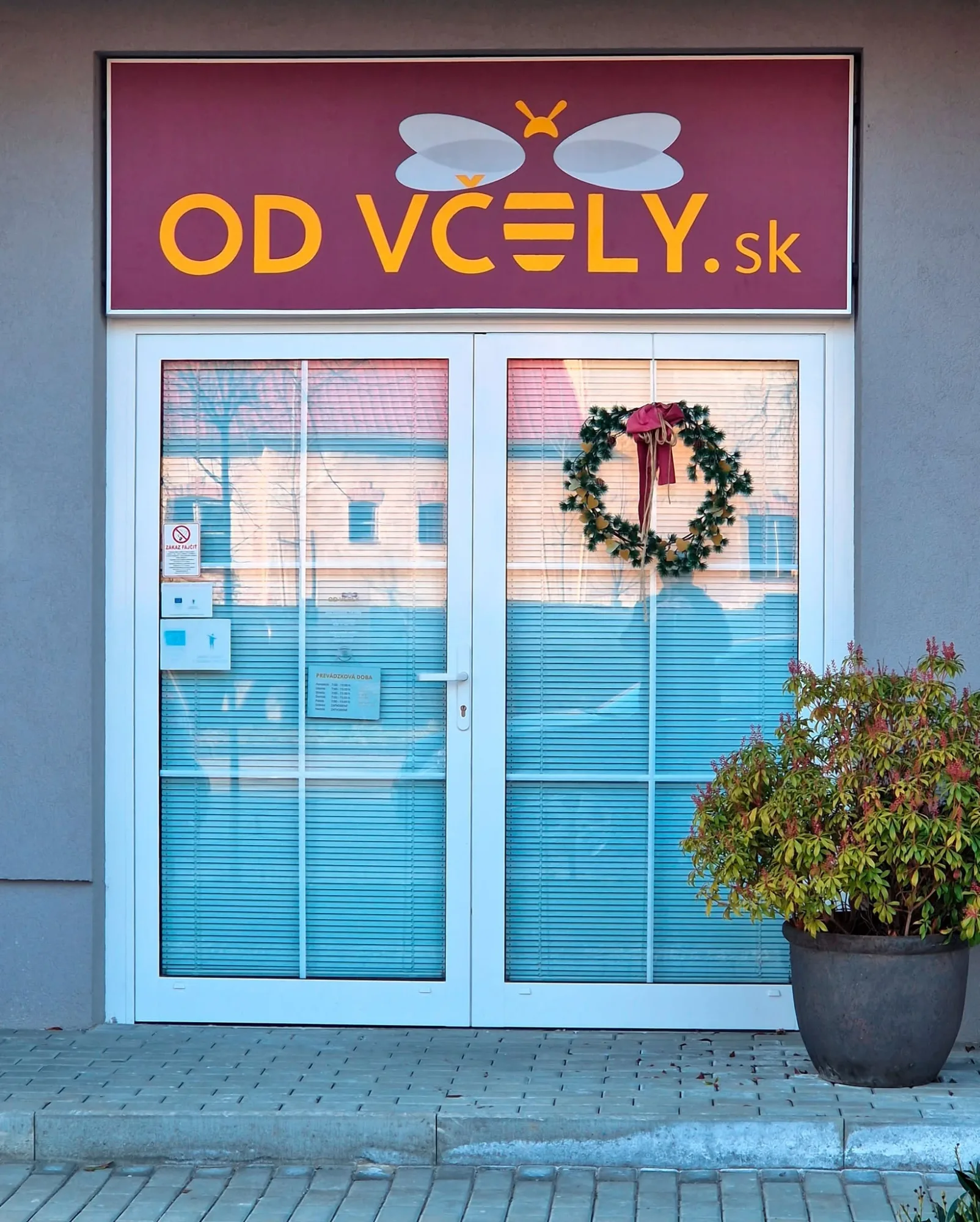 Bordový svetelný panel s logom včely a nápisom Od včely.sk nad vchodom do predajne, denný záber