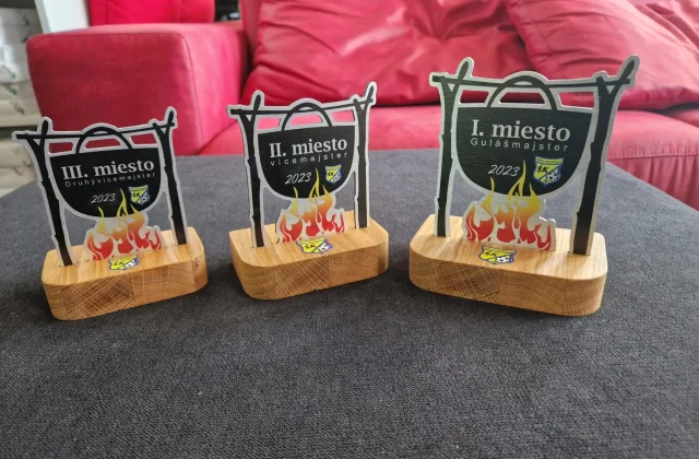 Tri trofeje v tvare kotlíka nad ohňom s brúseným kovovým povrchom a dubovými podstavcami